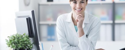 Attractive young female doctor leaning on the clinic reception desk with hand on chin, she is smiling at camera, medical staff and healthcare concept