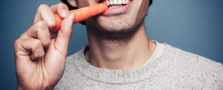 Young multi racial man is eating a carrot