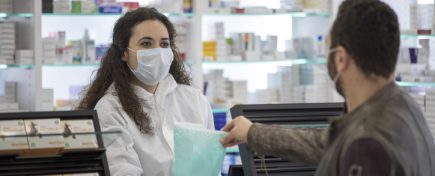 Female pharmacist wearing a surgical mask gives medication to the patient