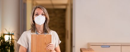 Young female receptionist holding clipboard folder with documents and with pandemic protection mask in hospital